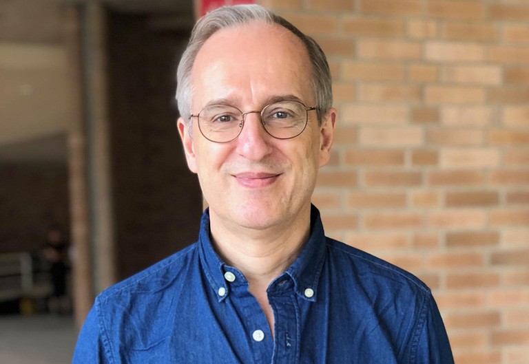 Smiling man with short light-coloured hair and wire-frame glasses.