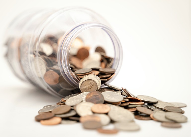 A transparent jar with coins spilling out of it.