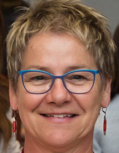 Middle-aged woman with short blonde hair and blue-rimmed glasses.