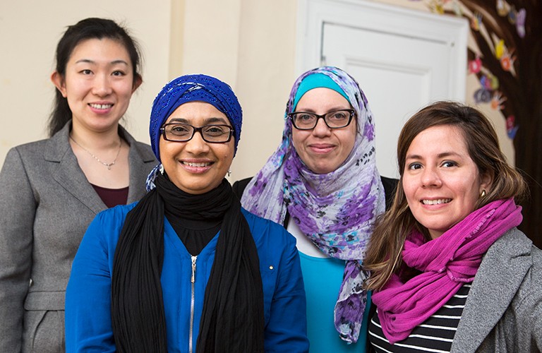 A group photo of four women, two wearing headscarves and glasses, and all smiling for the camera.