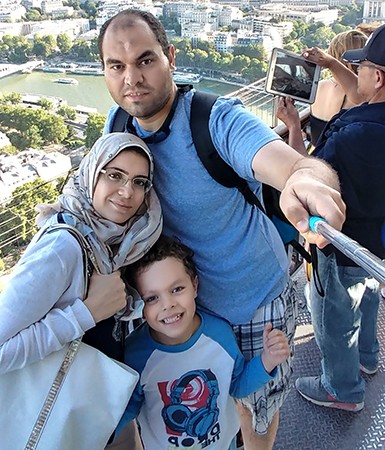 Portrait of a family — mother, father and young son — looking at the camera and up the top of a very high building.