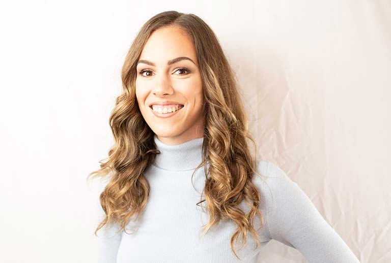 Young, smiling woman with light brown, long hair and a light grey sweater.