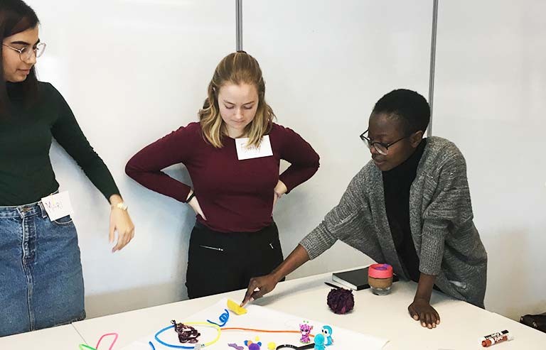 Emily Andrews (middle) and colleagues collaborating in the early stages of the project. Note: this image was taken pre-pandemic. A group of three young woman working on a project around a table.