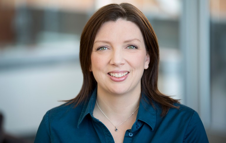 Smiling woman with long, dark hair, green eyes and a blue shirt.