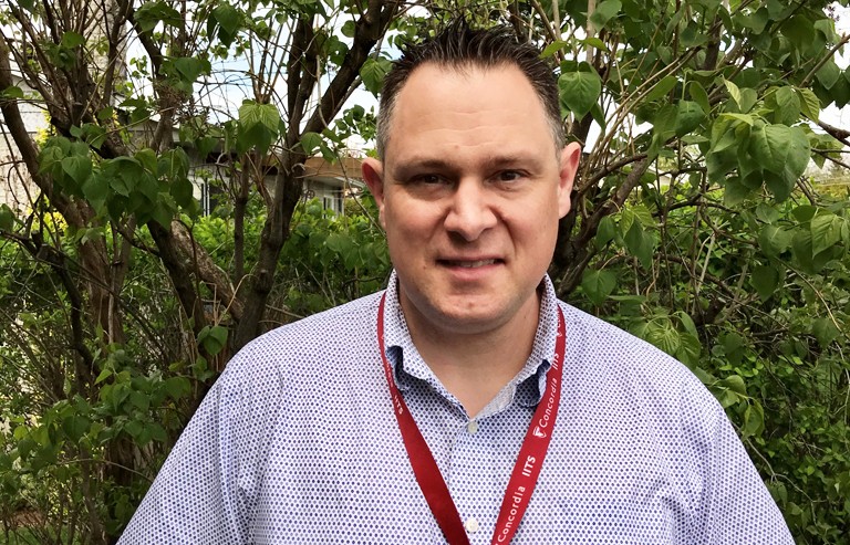 Man with short, gelled hair, a purple patterned shirt and a lanyard around his neck.