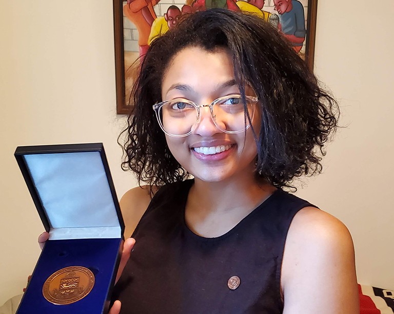 Smiling woman with see-through framed glasses and chin-length hair holding medal in blue case