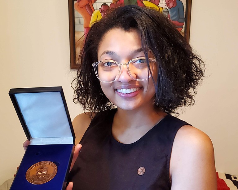 Celeste-Melize Ferrus Smiling woman with see-through framed glasses and chin-length hair holding medal in blue case
