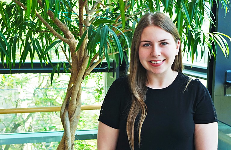 Young, smiling woman with long dark-blonde hair, red lipstick and a black short-sleeved top.