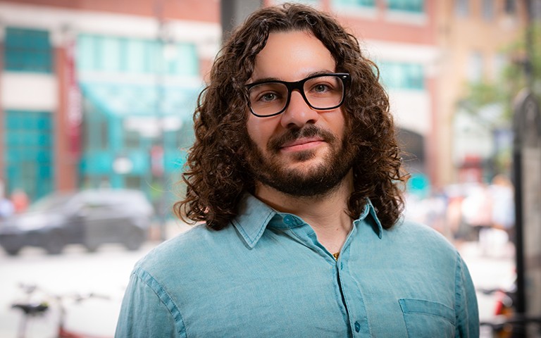Smiling man with long, curly hair, a beard, glasses and a green shirt.