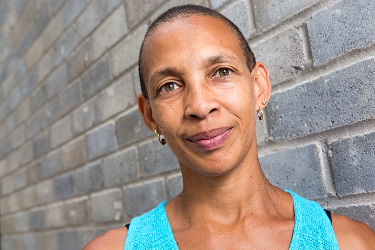 Smiling Black women with short hair, green eyes and a turquoise singlet.