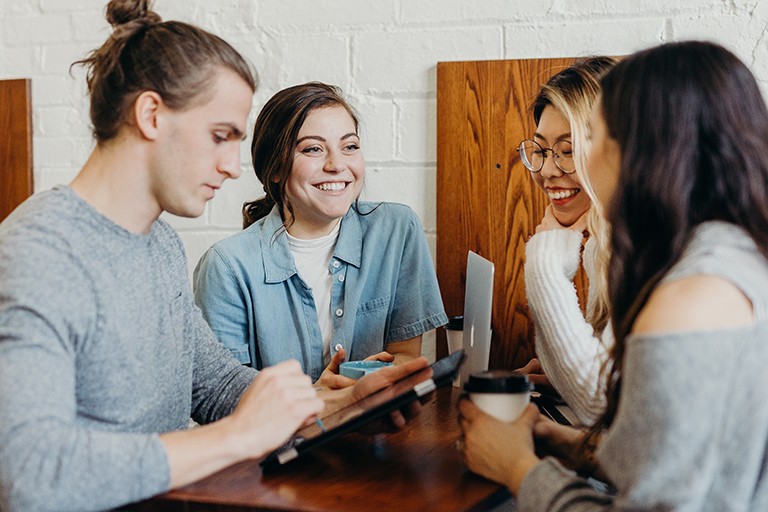 A group of smiling young people sitting around a table and talking together.