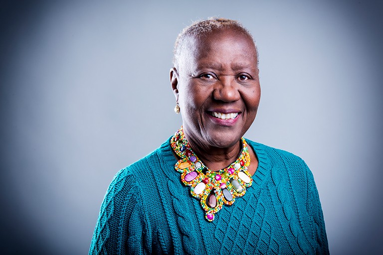 Smiling Black woman with a blue, ribbed sweater and a colourful necklace.