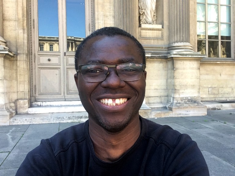 Smiling back man with glasses, sitting on the steps of an old building