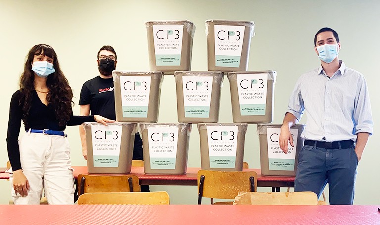 Three people in masks standing beside a table with a number of buckets, each with a label saying "CP3"