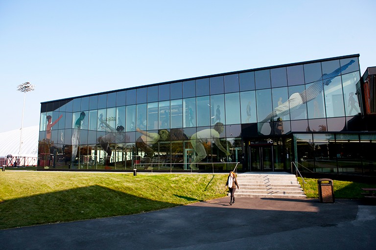 Photo of a building made of glass with a figure walking in the foreground.