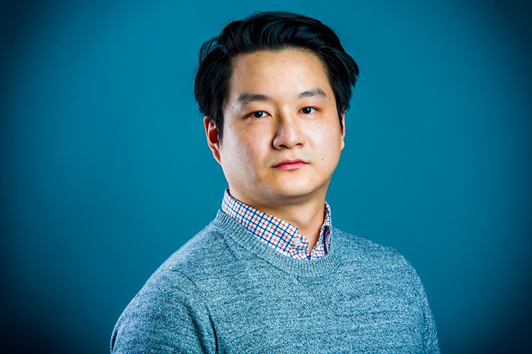 Young asian man with short, dark hair, a checkered shirt and a blue sweater.