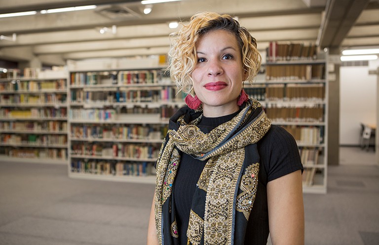 Young, smiling Black woman with curly, shoulder-length hair, in a library setting.