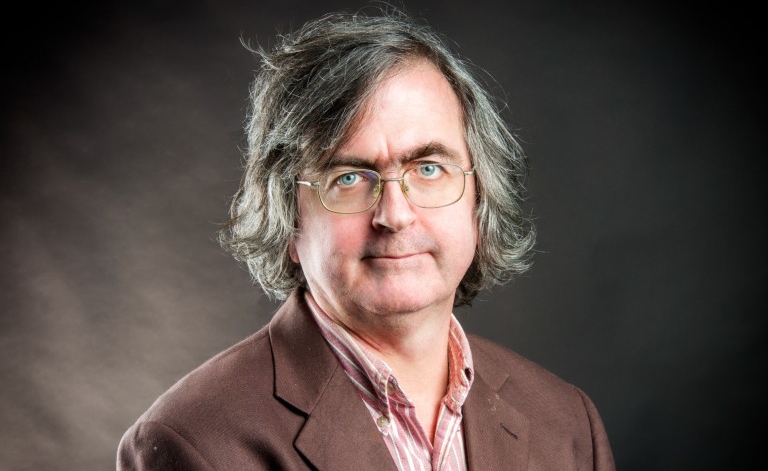 Man with glasses wearing brown blazer with striped button-up collared shirt