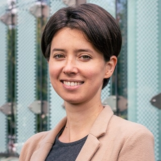 Young woman with short, brown hair, a salmon jacket and grey t-shirt.