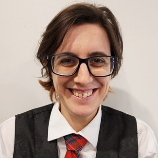 Person with short hair, dark-rimmed glasses, a white shirt, red tie and black vest.