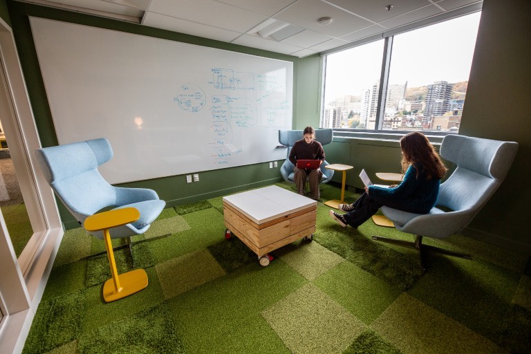 A carpeted open space with a moveable table and individuals working on chairs