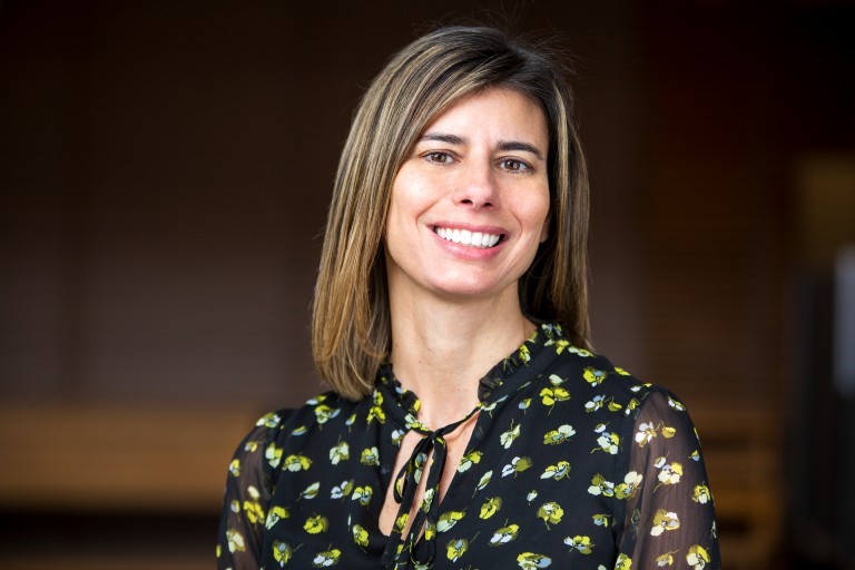 A woman smiles for a portrait wearing a black shirt with a butterfly design.