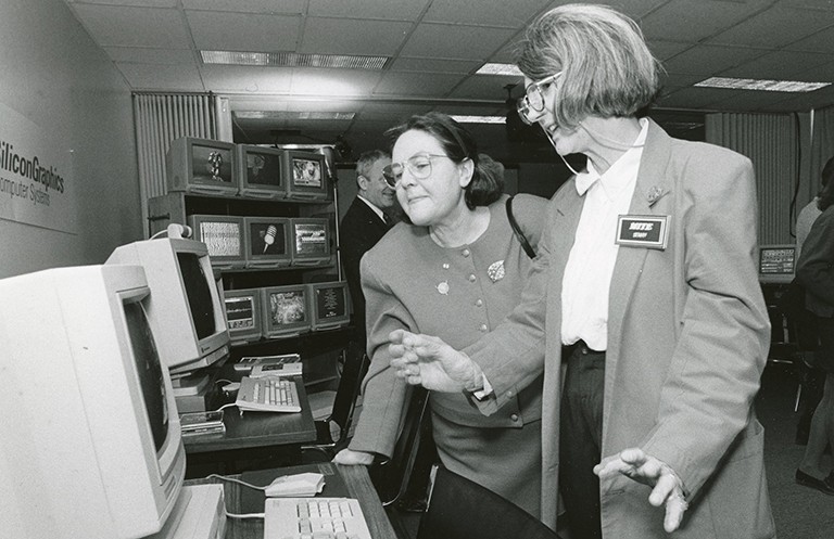 Archive photo in black and white of two women standing in front of a desktop computer.