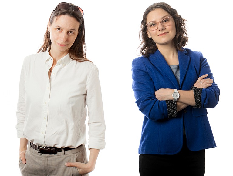 Two women standing side by side, both with long dark hair.