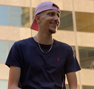 Young smiling man with a short beard, a backwards basketball cap, wearing a blue T-Shirt.