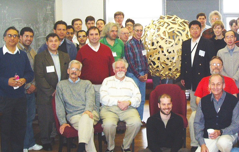 McKay, pictured centre, in a beige and white striped shirt, at a 2007 conference held in his honour. A group of people sitting and standing and smiling for the camera.