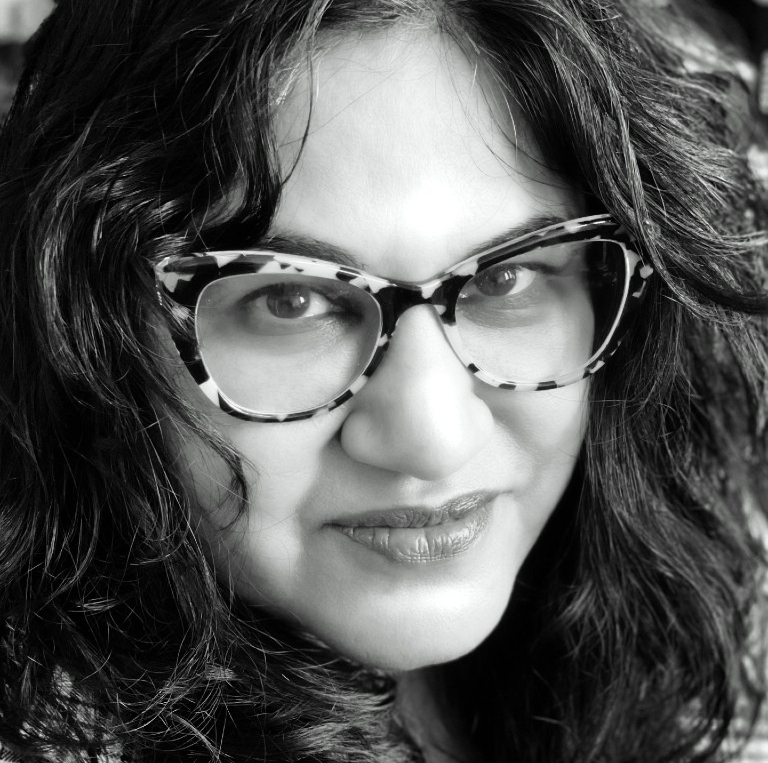Black-and-white headshot of woman with dark hair wearing glasses and plaid blazer