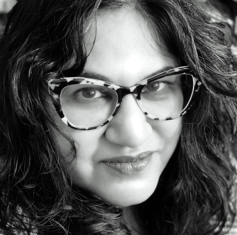 Nalini Mohabir Black-and-white headshot of woman with dark hair wearing glasses and plaid blazer