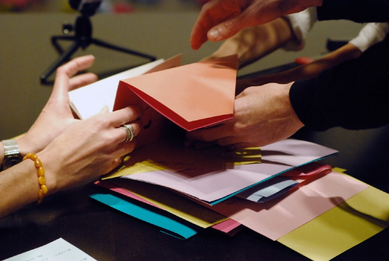 Two sets of hands sifting through colourful paper on a table