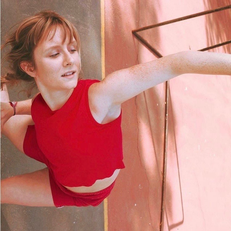 Woman with auburn hair in red outfit posing in a contemporary dance pose, leaning on one side with one arm raised