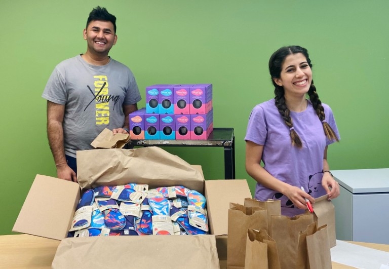 Two people standing behind table with box of reusable pads and menstrual cups on trolley