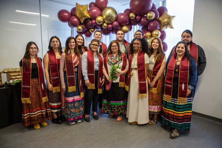 A group of indigenous graduates pose for a photo wearing the related regalia 