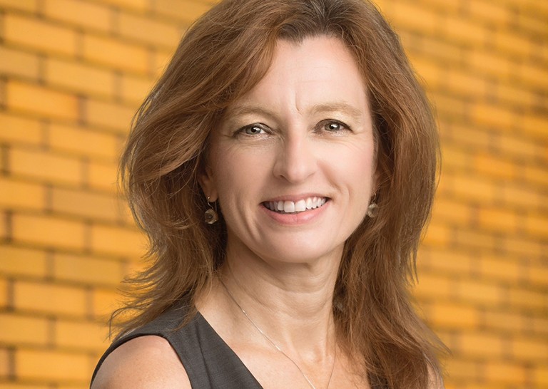 Smiling woman with long, brown hair, a sleeveless top and a gold necklace