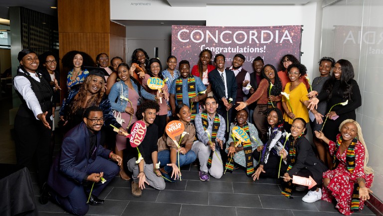 Group of students smiling and laughing in front of Concordia banner that says "congratulations!"