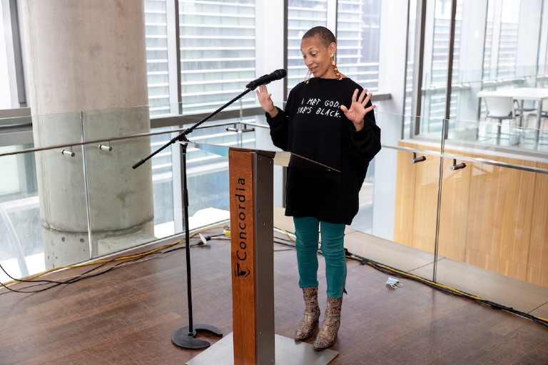 Woman speaking at podium wearing black long-sleeved shirt and teal pants Angélique Willkie