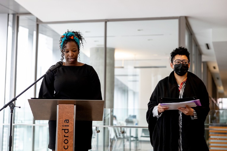 Woman at podium speaking with another woman holding documents