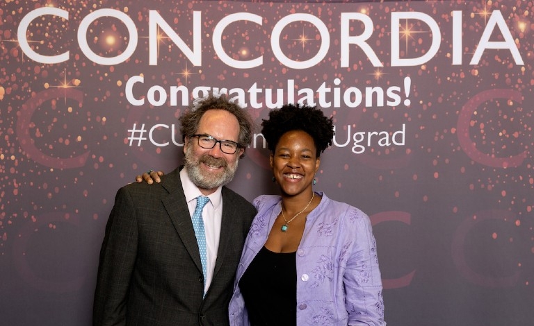 Andrew Woodall and Annick Maugile-Flavien Man wearing blazer with sky-blue tie and woman wearing lilac blouse and blue necklave and earrings