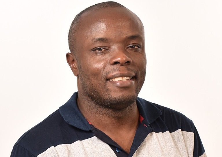 Isaac Blaise Djoko: A smiling Black man with close-cropped hair and wearing a striped polo shirt.