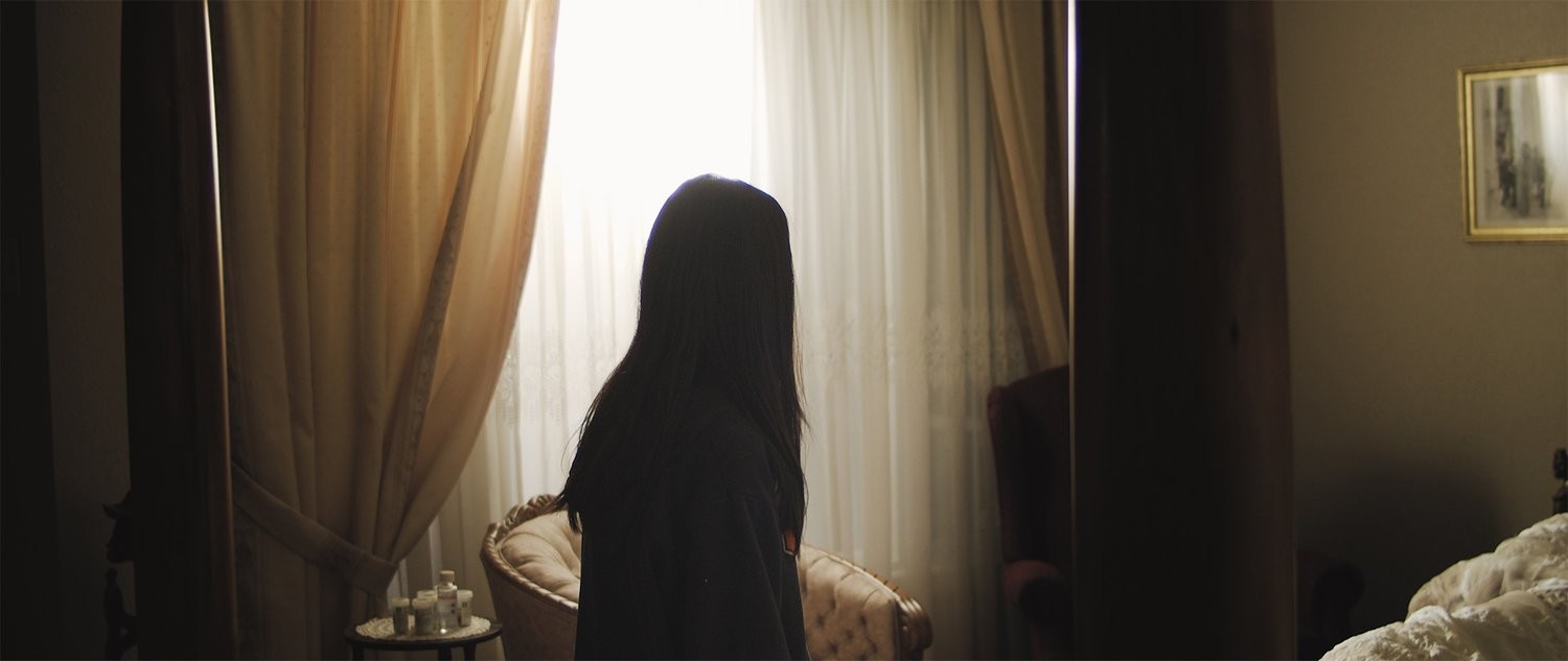 Woman with long dark hair walking in lowly lit bedroom