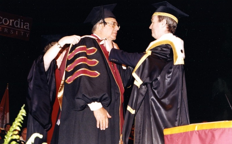 Man in graduation gown receives honorary degree at ceremony