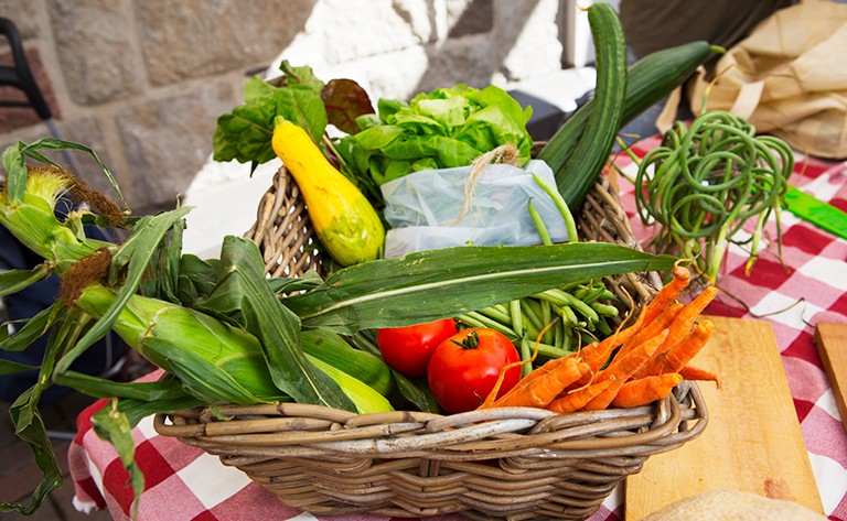 A basket of fresh vegetables, like tomatoes, corn, green beans and carrots.