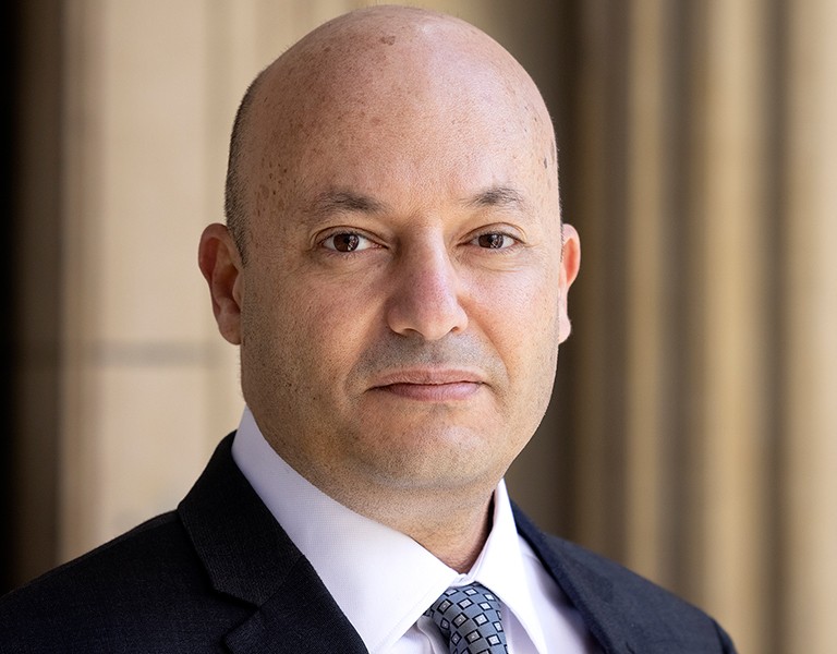 Slightly smiling bald man with brown eyes, wearing a dress shirt, tie and suit jacket.