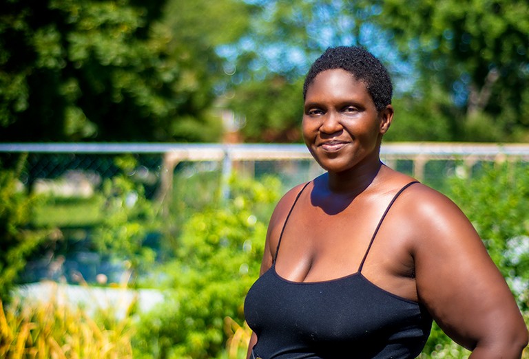 A smiling Black woman wearing a singlet and standing in a community garden.