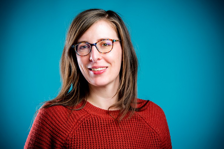 Smiling woman with long, light brown hair, red-rimmed glasses and wearing a red knit sweater.