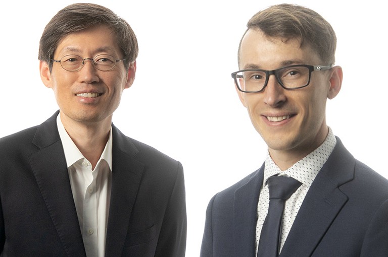 Two men in suits, a smiling Asian man on the left with wire-rim glasses and a smiling white man on the right with black-rimmed glasses.