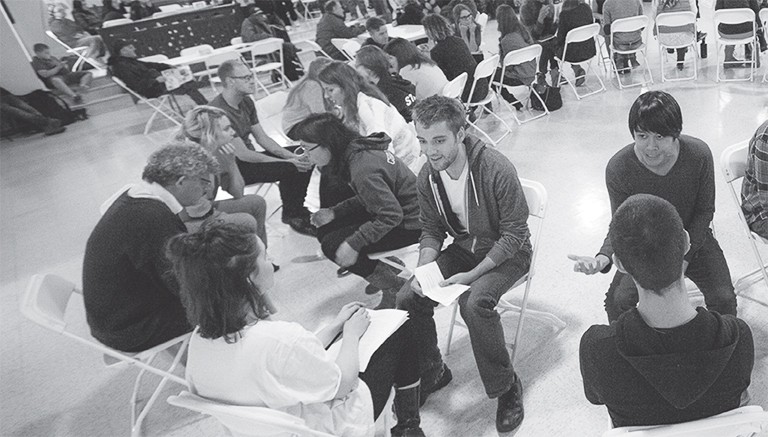 A group of people sitting in folding chairs and paired off, talking animatedly to one another.